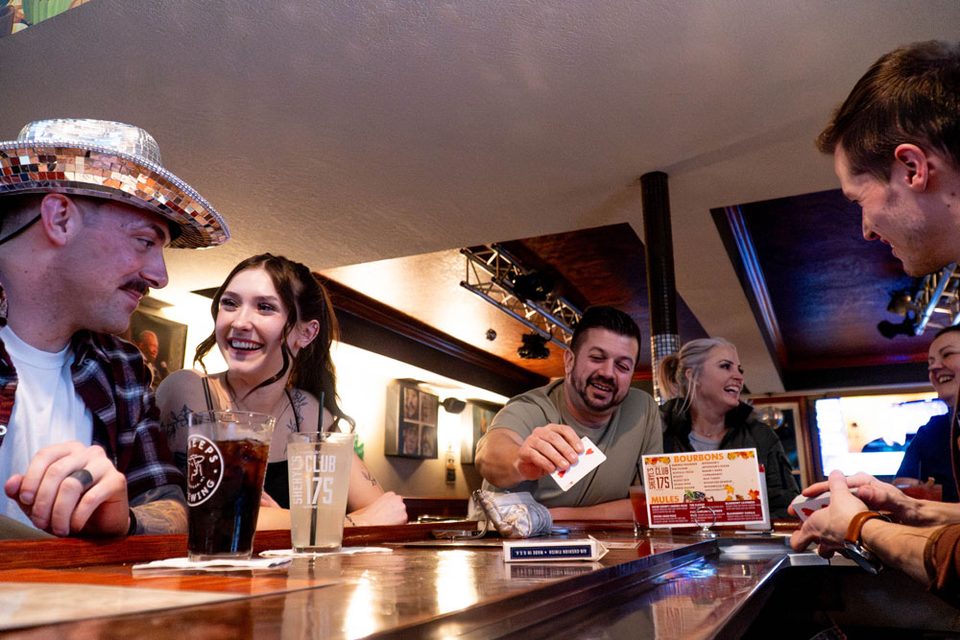 Guests laughing as Caleb Hyatt performs a card trick across the bar at Sheryl's Club 175